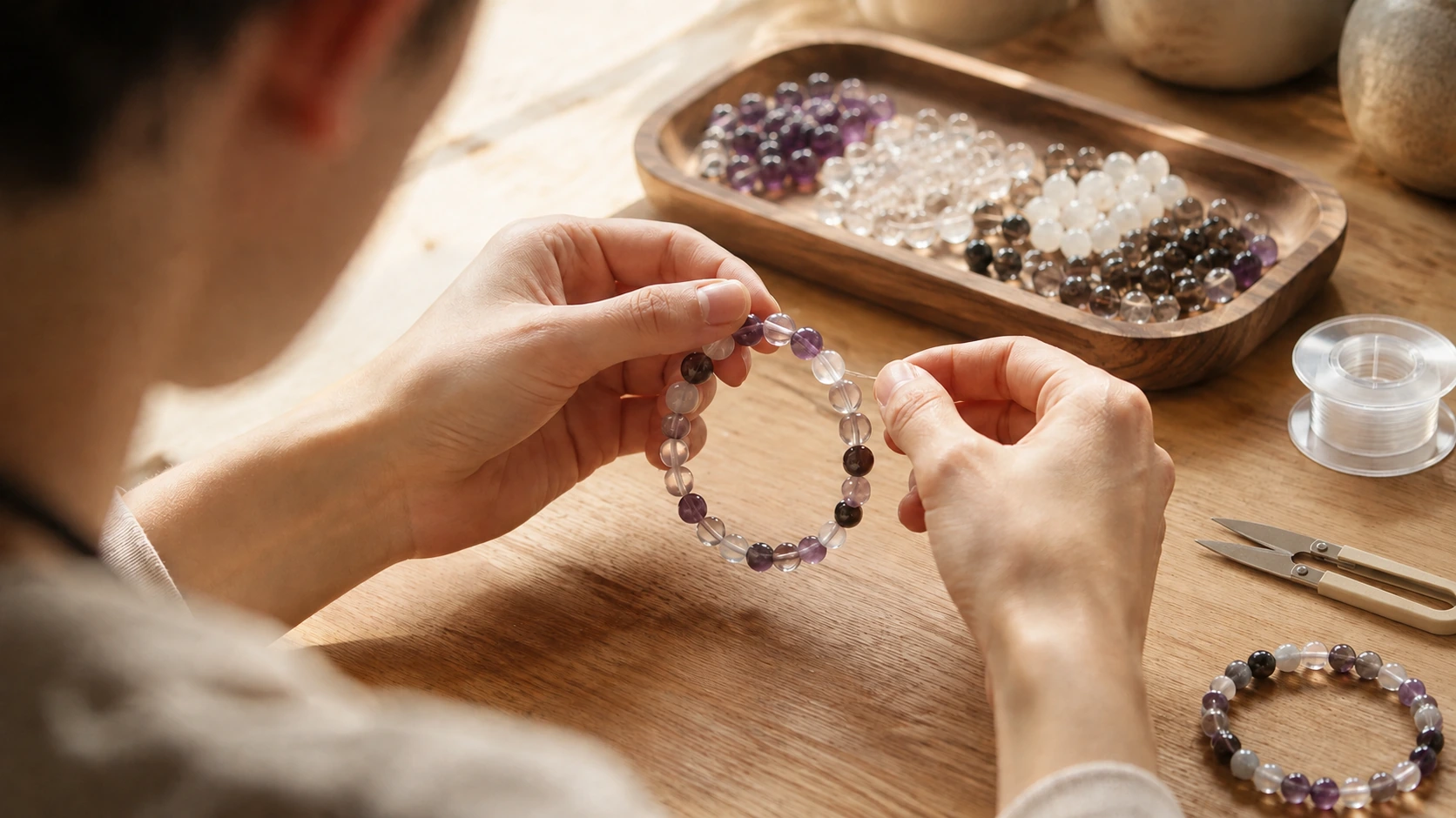 Hands threading an amethyst bead onto clear elastic cord